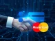Two hands, one representing Ripple and the other Mastercard, shaking over a digital blockchain network, symbolizing the partnership to enable credit card settlements on the XRP Ledger.