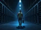 Bitcoin miner exodus depicted in a photorealistic data center scene with a technician leaving inactive mining rigs.