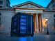 Blockchain server nodes in front of traditional bank building representing financial institution digital assets transition.