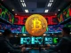 Bitcoin coin on a trading desk with multiple monitors showing market data and liquidation charts