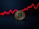 Bitcoin coin on a dark surface with a red downward-trending chart, illustrating bearish market analysis.