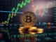 Bitcoin coin on a digital display showing BTC price near $79,000 with green market charts in the background.