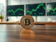 Bitcoin coin on table with stock market monitors in background, representing Bitcoin rally extends but BTC options price uncertainty