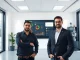 CopilotKit co-founders Atai Barkai and Uli Barkai standing in front of a digital screen displaying interactive AI agent user interfaces.