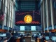 Wall Street trading floor with cryptocurrency price charts on a large digital display