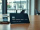 A modern crypto-linked credit card on a wooden table with a smartphone showing a payment confirmation.
