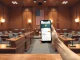US Senate committee hearing room with a smartphone showing a crypto exchange app in the foreground