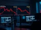 Bitcoin price chart showing sharp decline to $72,600 on trading desk monitors with red candlesticks