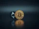 Ether coin trailing behind a Bitcoin coin on a reflective surface, representing market underperformance.