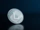 Silver Litecoin coin on dark reflective surface with soft lighting