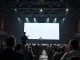 Founder presenting on stage at a tech conference with a large audience watching.