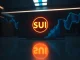 Sui crypto SUI token symbol on a digital display with blue and orange lighting for a financial news article.