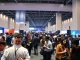 Attendees networking at a large tech conference hall with exhibition booths and stage lighting.
