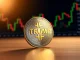 A gold TRUMP coin resting on a wooden surface with a blurred financial chart in the background.