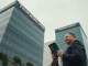 Trump Media headquarters building with a person looking at a smartphone showing a Bitcoin chart and ETF symbol.