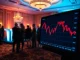 Trump memecoin price chart showing a decline, with a blurred exclusive investor gala in the background.