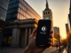 Person holding a smartphone with a digital wallet near the Bank of England building in London during golden hour.
