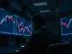 Trader observing Ethereum price drop on multiple monitors in a dimly lit trading floor