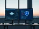 Two computer monitors in a modern Asian tech office displaying AI software interfaces, one with a blowfish icon and one with a shield icon.