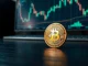 Bitcoin coin on wooden table with blurred trading chart in background