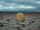Bitcoin coin resting on cracked dry earth under overcast sky, representing market uncertainty.