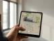 Person holding a phone showing a Google Earth satellite map with an AI-generated building overlay