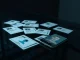 A dark desk with scattered identity documents and a smartphone showing a facial recognition interface, illustrating a data breach.