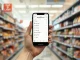 Person holding a smartphone with a shopping list app inside a grocery store aisle