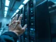 Human hand reaching toward a server rack in a high-tech AI lab, symbolizing control of superintelligence.